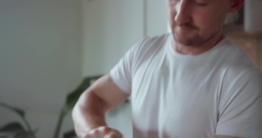 A man in a kitchen uses a hand grinder for coffee beans