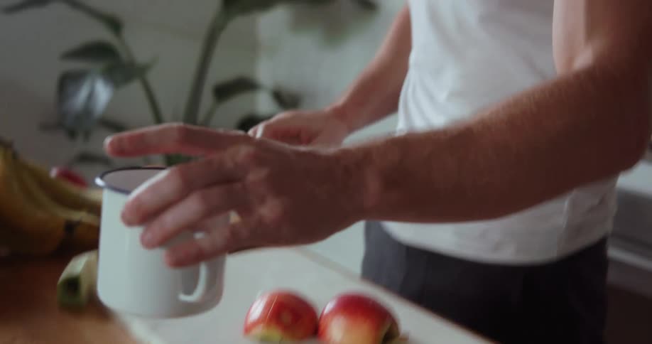 Man chops fruit on a cutting board and takes a drink out of a mug
