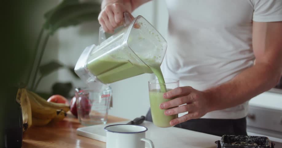 A man makes a smoothie in a blender and pours it into a glass