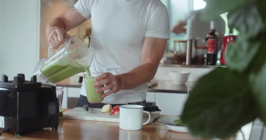 A man pours a green smoothie in a glass