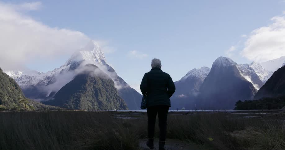A person hikes over the grass towards a mountain