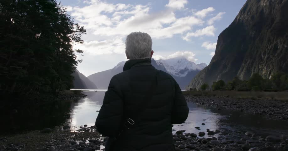 A woman stares out at a lake below a mountain