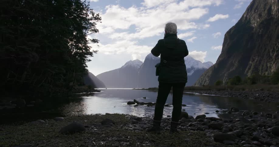 A woman in a puffer jacket takes a picture of a lake