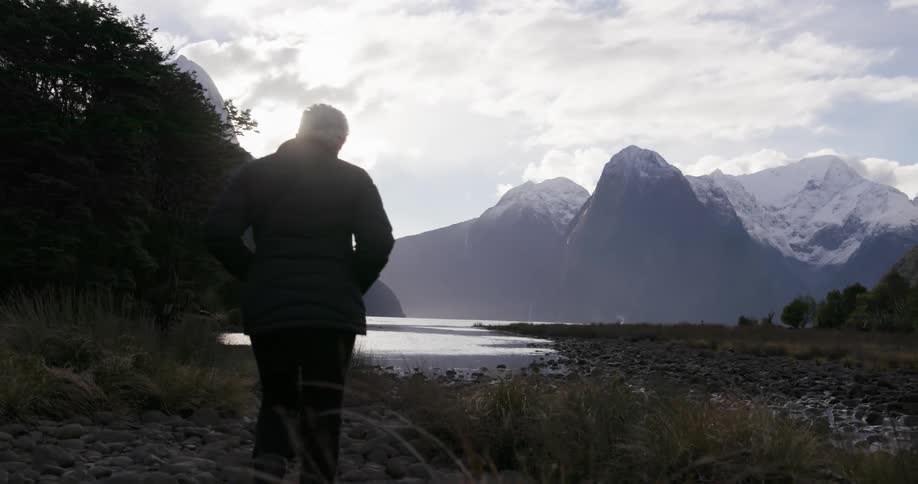 A woman approaches the lake below the mountains