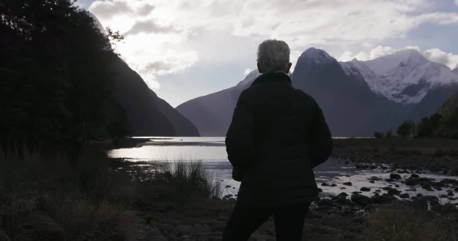 A person stands near the lake on a cloudy day