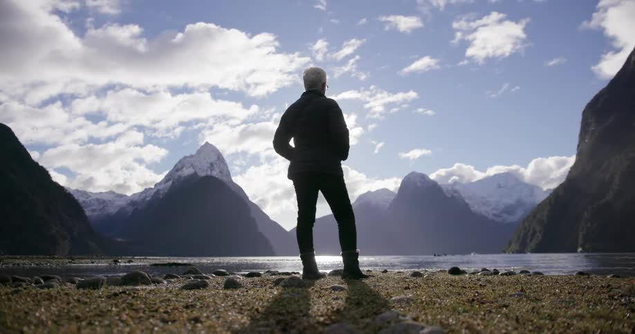 A woman stands in front of a flowing lake in front of mountains