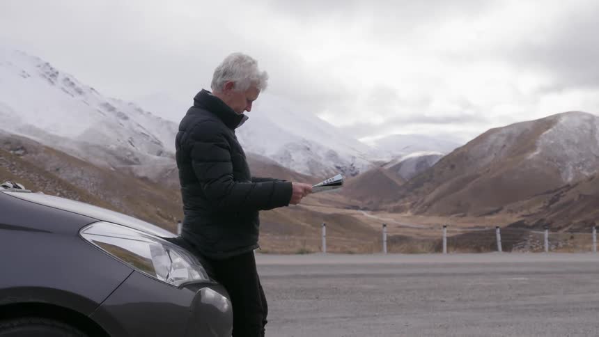 A woman leaning on her car studies a map