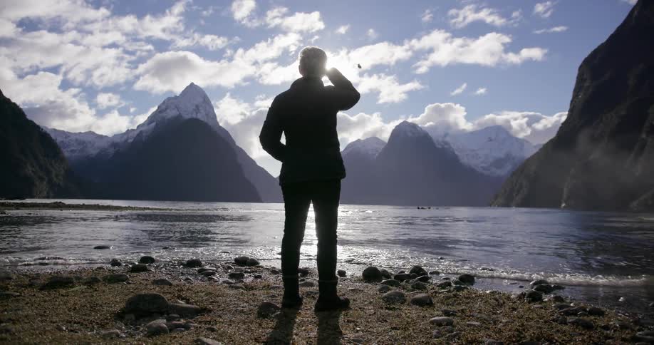 A woman watches a helicopter fly over mountains