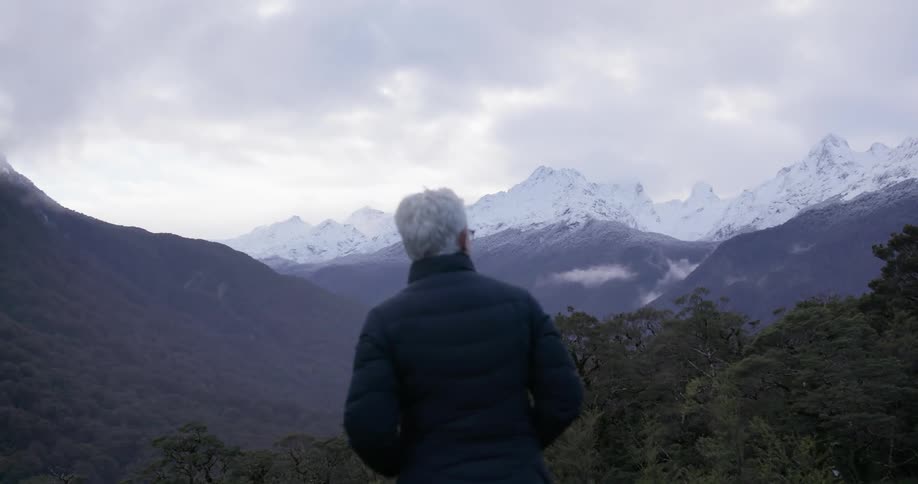 A woman looks out towards snow covered mountains