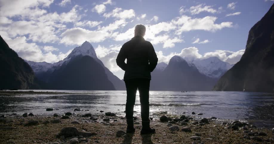 Person stands at the edge of a lake looking out at the mountains