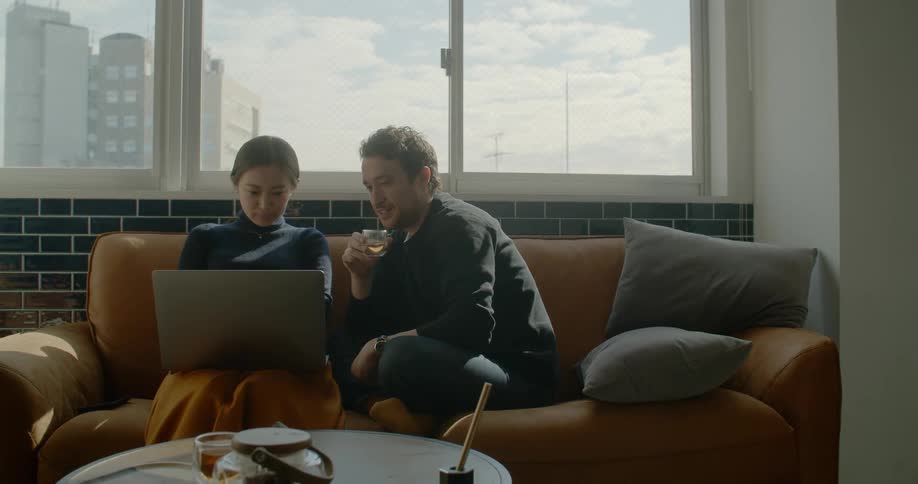 A man and woman sit on a couch together looking at a laptop