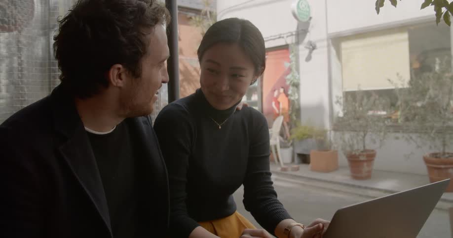 Asian woman and white man sitting at the table uses a laptop in the cafe