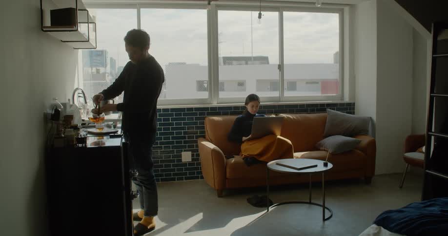 A man makes coffee while a woman sits on a couch