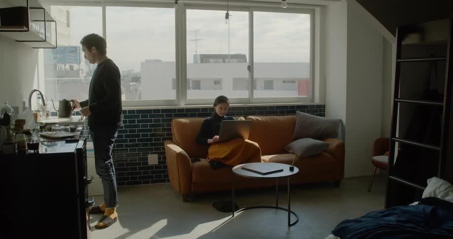 A man pours tea as a woman sits on the couch on a laptop