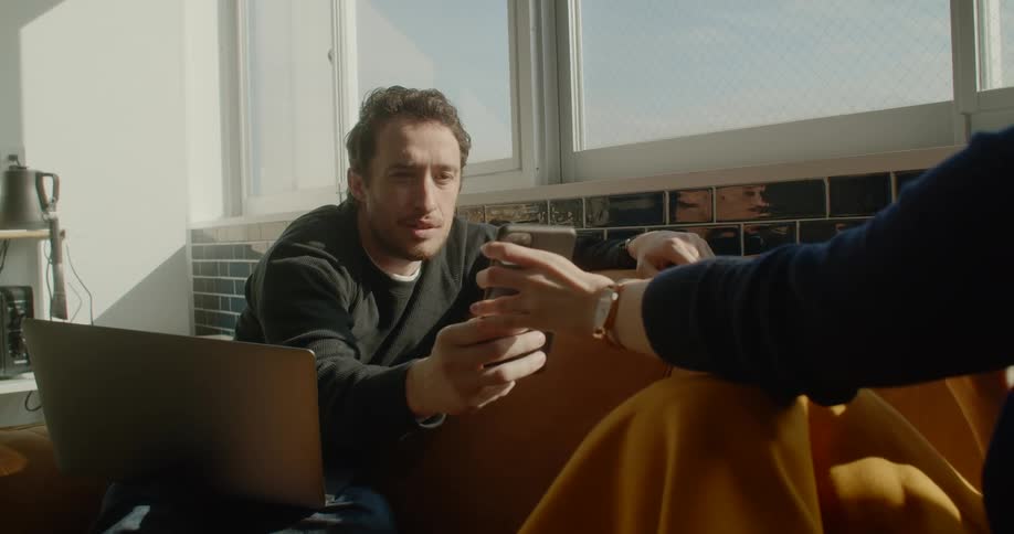 Two people sit on a couch and look at a cell phone