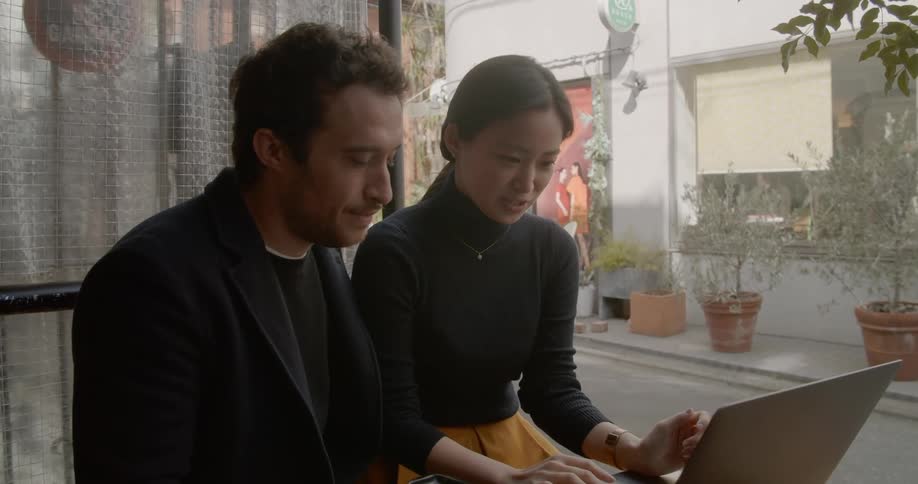 A man and woman sit and drink coffee while looking at a laptop