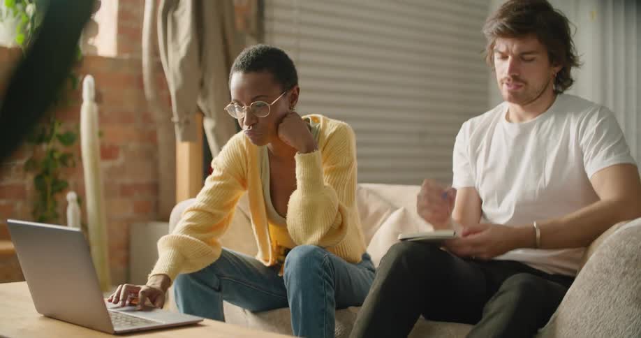 A man and woman are sitting indoors and looking at a laptop