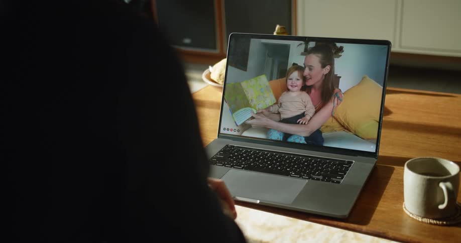 Man with a black sweater makes a video call on a laptop with his wife and daughter at home