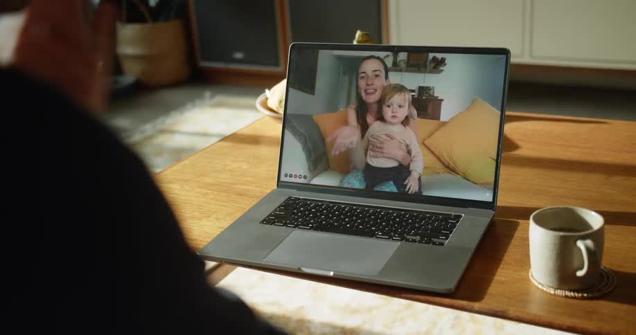 Woman and a baby on a computer screen sitting at home in their living room waving goodbye to the person on the other side of the camera