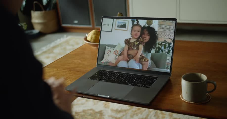 A woman and child wave from the screen to a person video chatting them from a laptop
