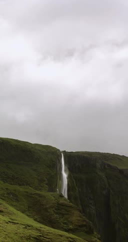A river falls from from the top of a cliff into a canyon under a cloudy sky