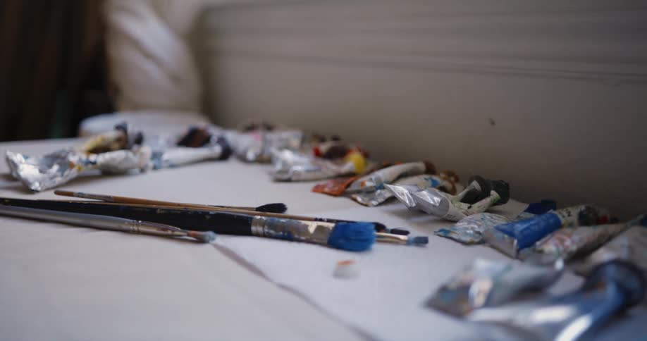 Tubes of paint and paint brushes sit by a window in a house