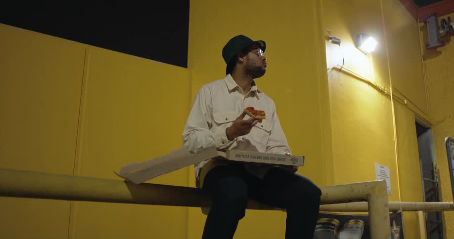 A man is eating pizza while sitting outside of a building