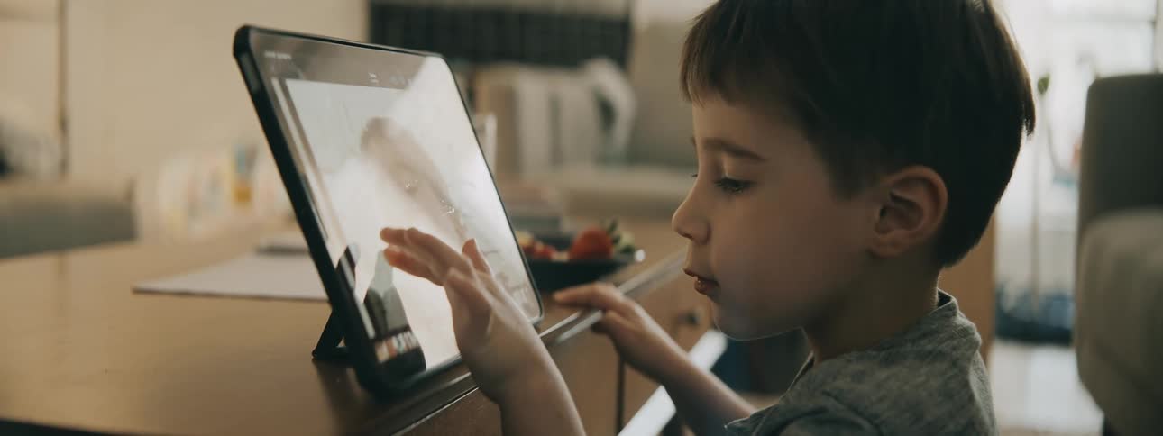 Boy sitting on floor in living room smiles while using tablet set on coffee table