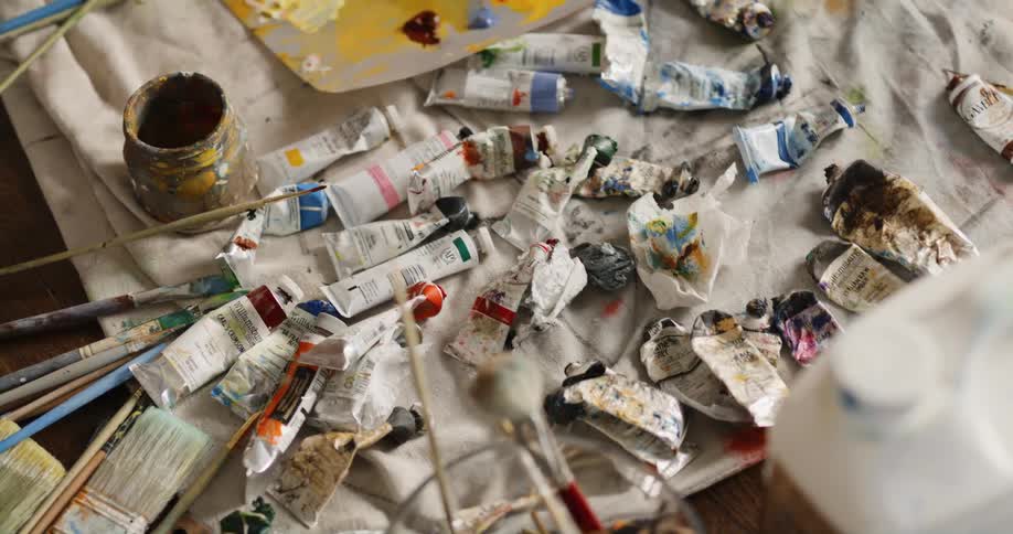Paintbrushes and tubes of paint lying atop a cloth on a table