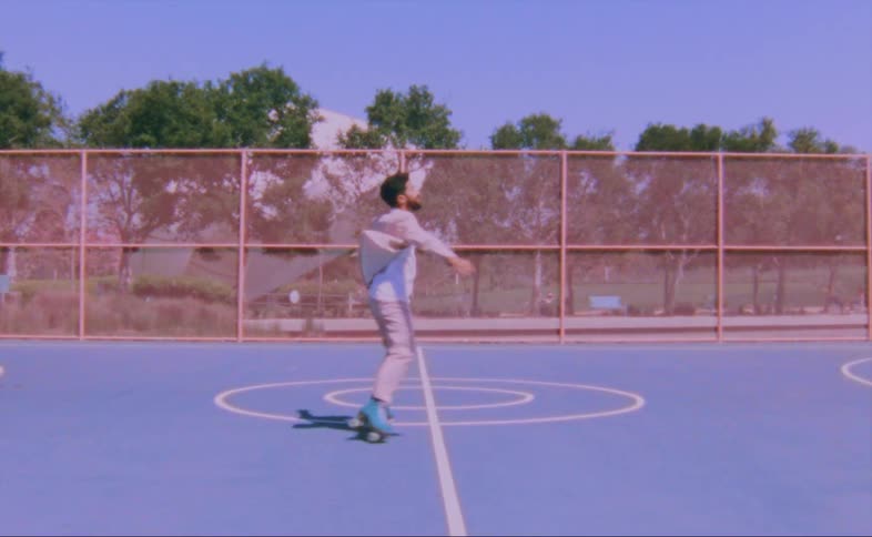 A man wearing a pink jacket and pink pants is dancing on roller skates on an outdoor basketball court