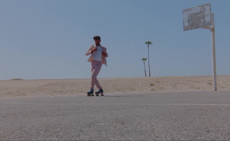A man wearing a pink jacket and pants is dancing on roller skates on a basketball court near a beach