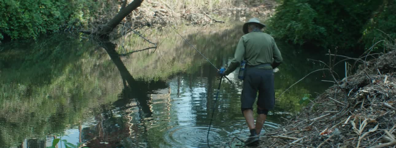 A man who is hiking tests the water of a river before stepping in