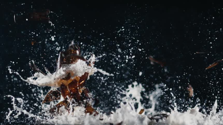 Beer bottles falling in slow motion and breaking against a black background