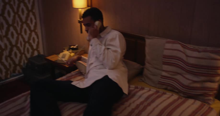 A man talks on the phone while lying in bed in a hotel