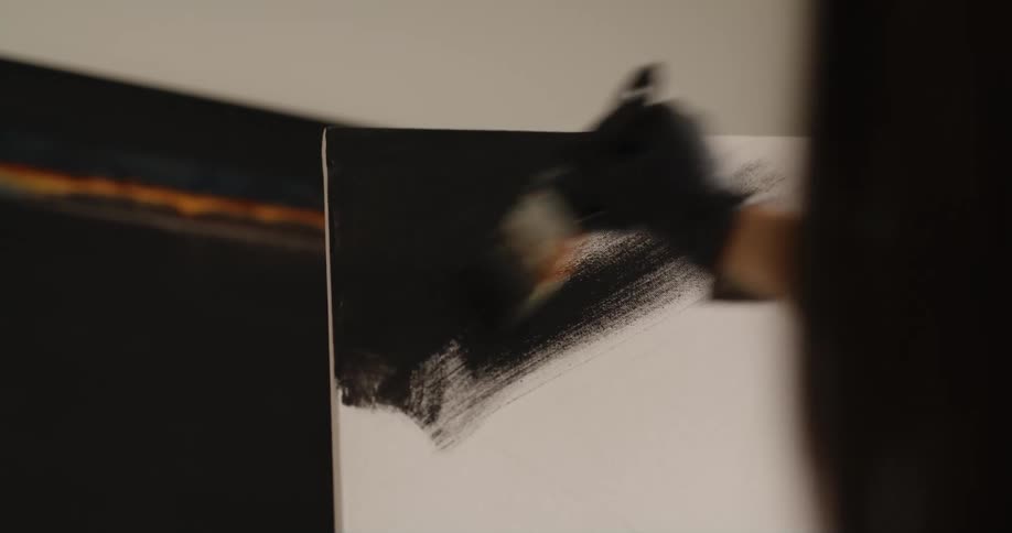A painter uses a paintbrush to spread black paint on a canvas