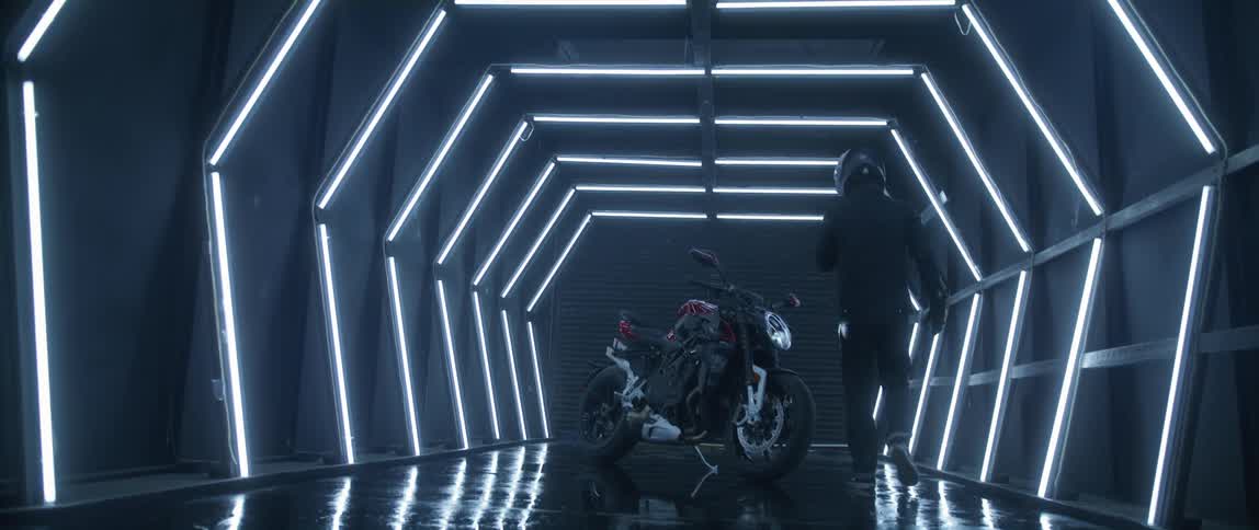 A man walks through a well lit hallway and climbs onto a motorcycle