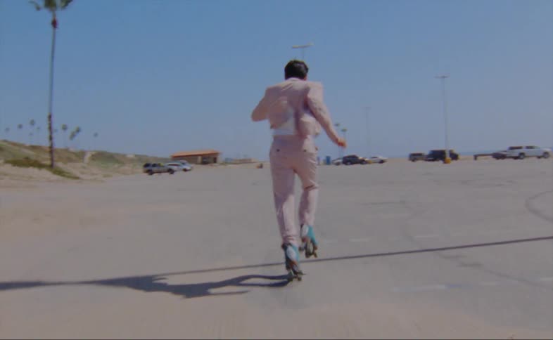 A man wearing a pink jacket and pants is dancing on roller skates in a parking lot