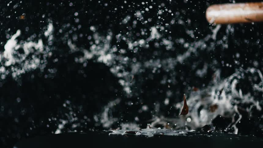 A beer bottle is destroyed with a baseball bat