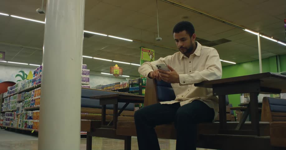 Man sits on bench in grocery store scrolling on his sell phone