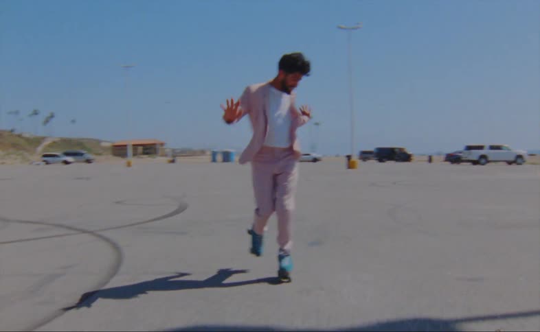 A man wearing a pink jacket and pants is dancing on roller skates in a parking lot