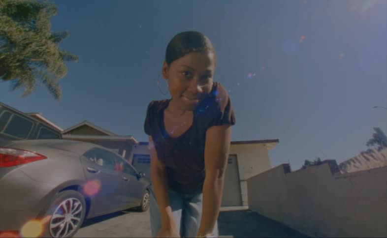A young woman poses in front of a camera in the driveway of a house on a clear day
