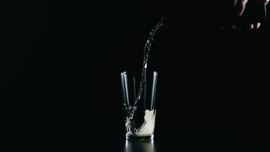 A person is pouring a liquid into a glass on a table