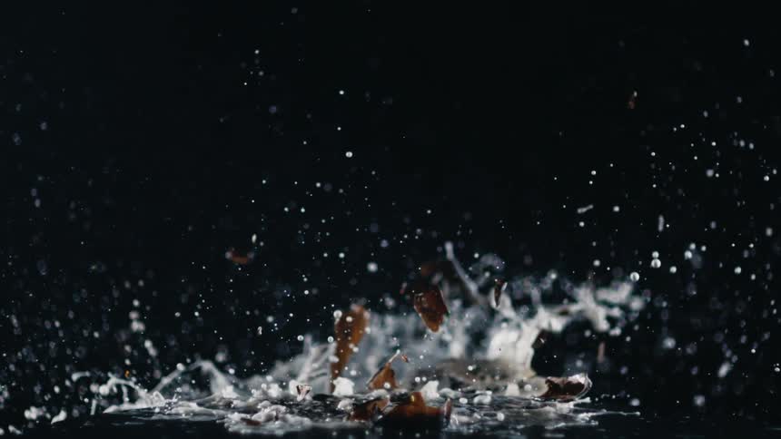 A glass bottle sits on a table as a crowbar smashes it and liquid splashes and flies
