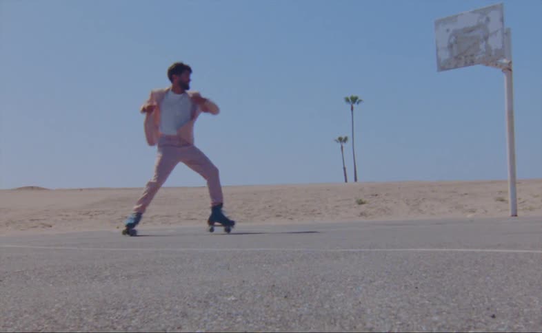 A man wearing a pink jacket and pants is dancing on roller skates on an outdoor basketball court