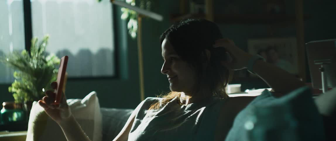 Woman sits on couch smiling and talking on a smartphone video call