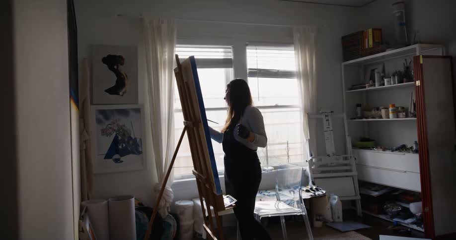 A woman is standing in a room painting on an easel