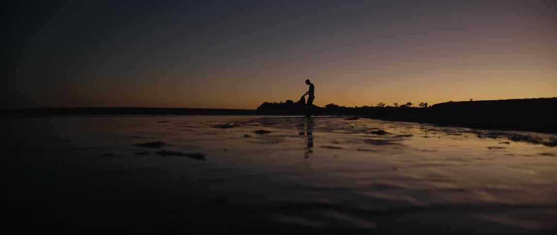 A man walking on the shore as the sun sets
