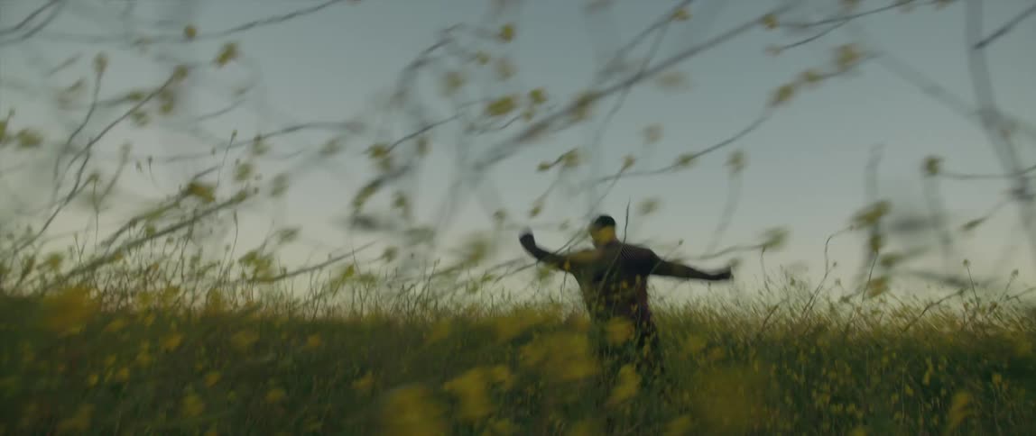 A man is running in a field filled with tall grass and plants and buttercups