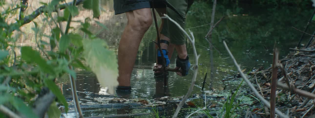 A man ties twigs together while standing in a creek