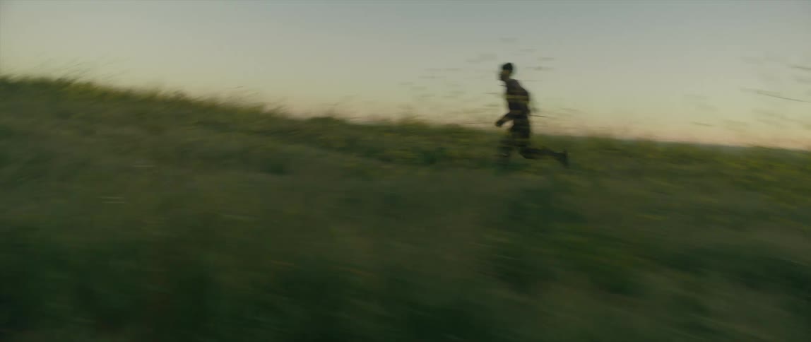A young man running across a field of flowers keeps nervously looking behind him